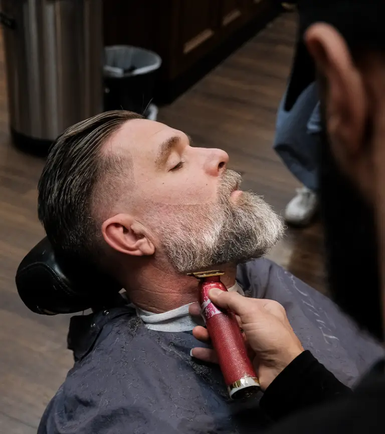 en äldre man som får sitt skägg trimmat hos sin barberare i stockholm