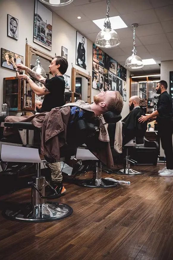 två barberare i en Tailor's Barber barbershop i stockholm som utför behandlingar på varsin kund.