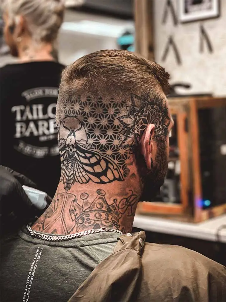 Barberare som får en behandling. han har tatueringar i nacken. ett motiv av en fjäril och geometriskt mönster.