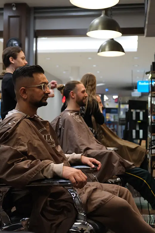 Kunder på Tailor's Barber sitter i barberarstol och får sitt hår & skägg klippt av herrfrisör i Stockholm.