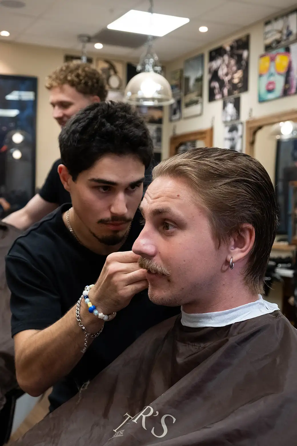 Barberare trimmar mustasch och mellanlångt hår på kund hos Tailor’s Barber i Stockholm City.