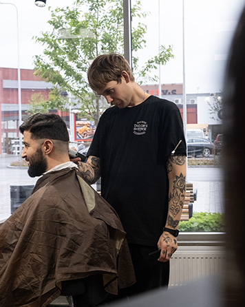 Barberare som klipper en kund i sidoprofil under en herrklippning hos Tailor’s Barber