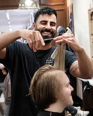 Leende barberare klipper långt hår på en kund i barbershop.
