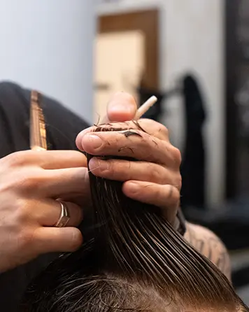 Närbild på barberare som klipper hår med sax och kamm