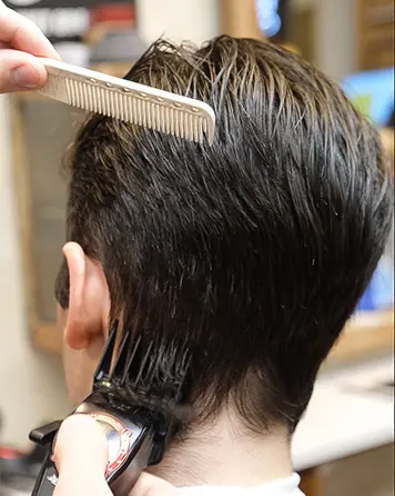 Barberare klipper en taper fade i nacken med maskin och kam.